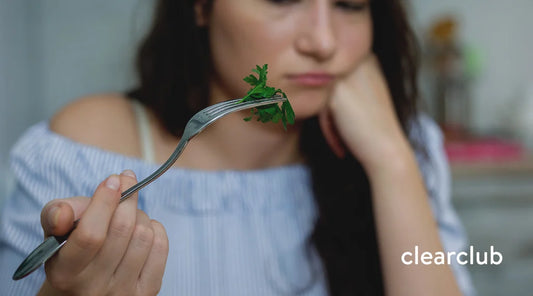Woman making a displeased face while looking at a leafy green vegetable on her fork.