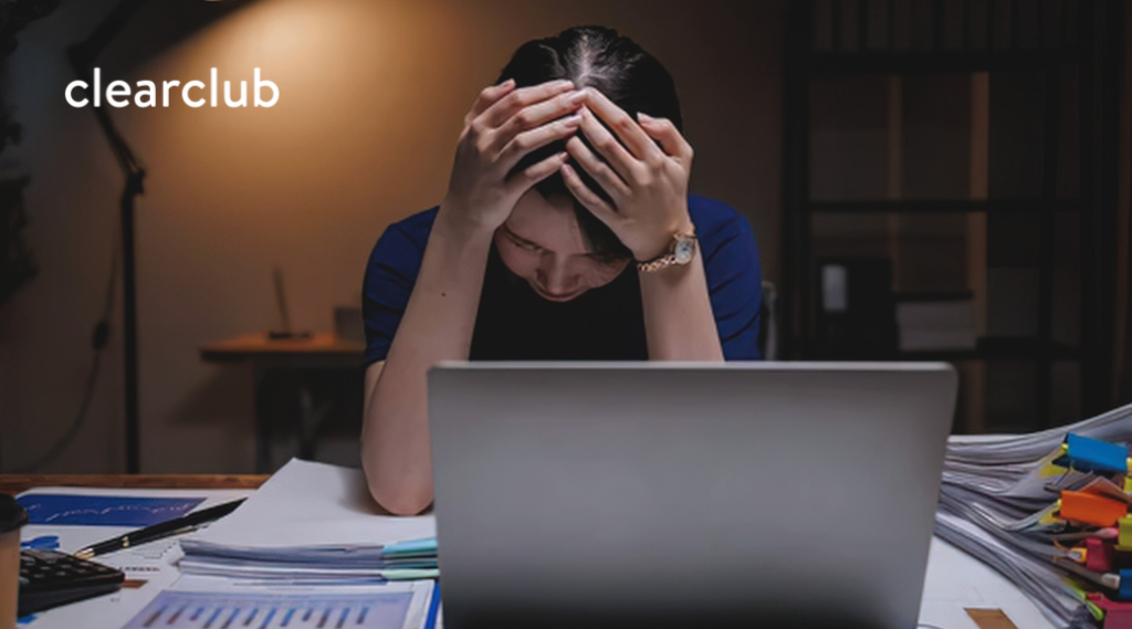Woman holding her temples while sitting at a laptop, showing possible headache and jaw tension from prolonged desk work.