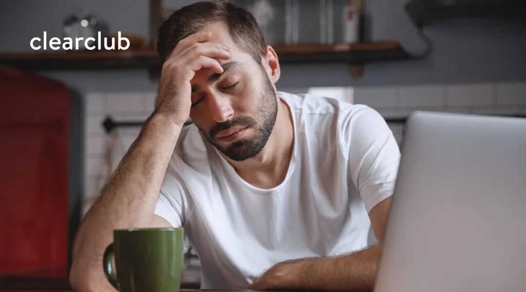 Man holding his forehead while working at a desk, appearing to experience a headache or work-related stress