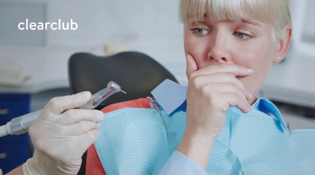 Woman experiencing dental anxiety as a dentist holds a dental tool