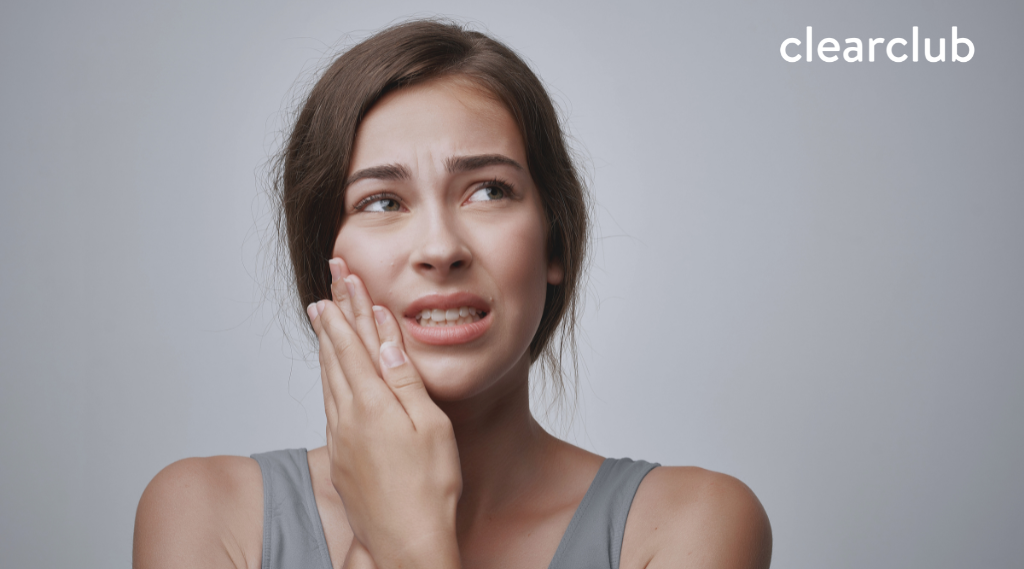 Woman holding her cheek with a pained expression, indicating discomfort caused by wearing retainers.