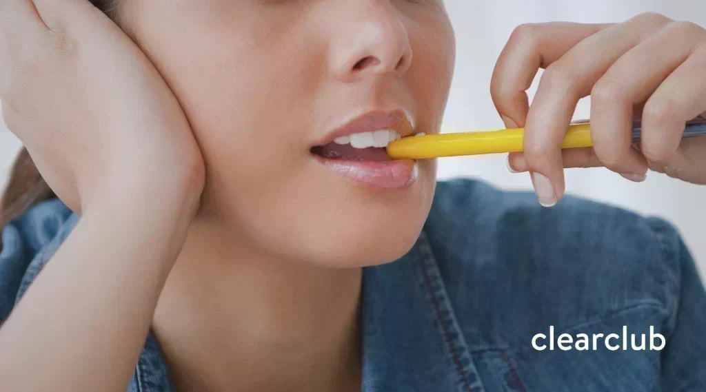 Woman biting the tip of a pen, an oral habit that can affect orthodontic results