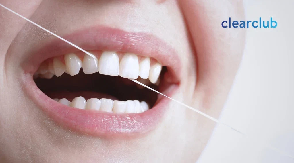 Person flossing between her front teeth as part of a retainer care routine 