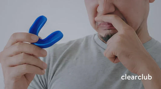 A man reacting to an unpleasant taste while holding a blue mouthguard.
