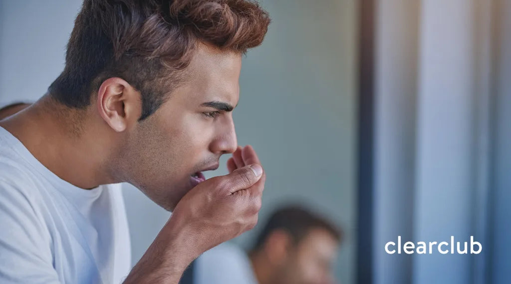 Man checking his breath by cupping his hand near his mouth, concerned expression, with ClearClub logo in the corner