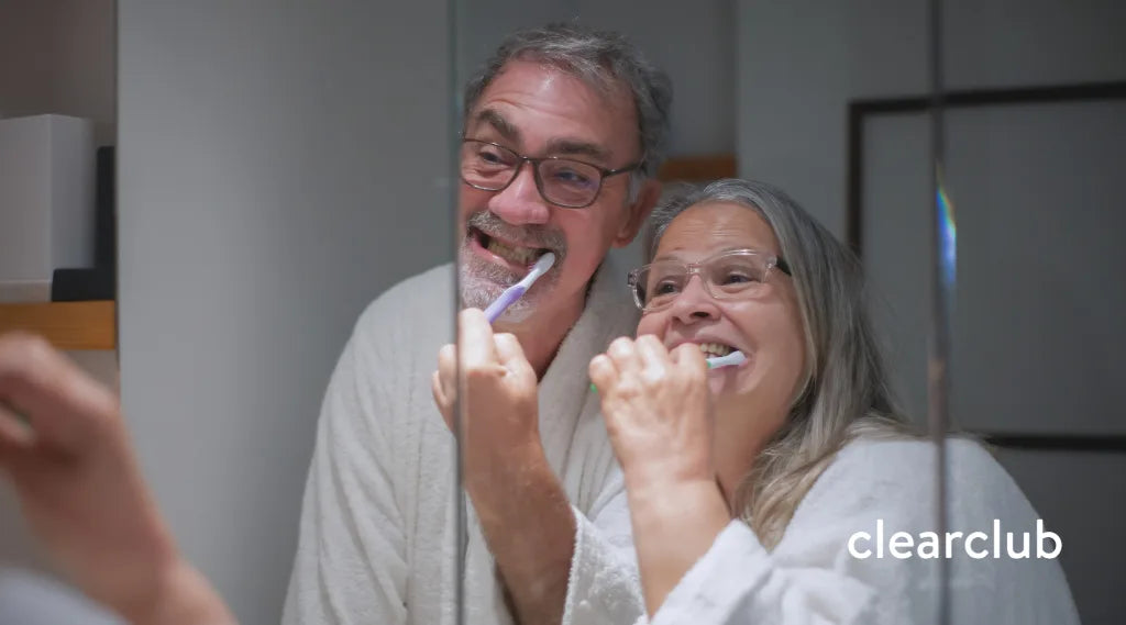 Two older adults brushing their teeth together to maintain oral hygiene and reduce stain-causing bacteria.