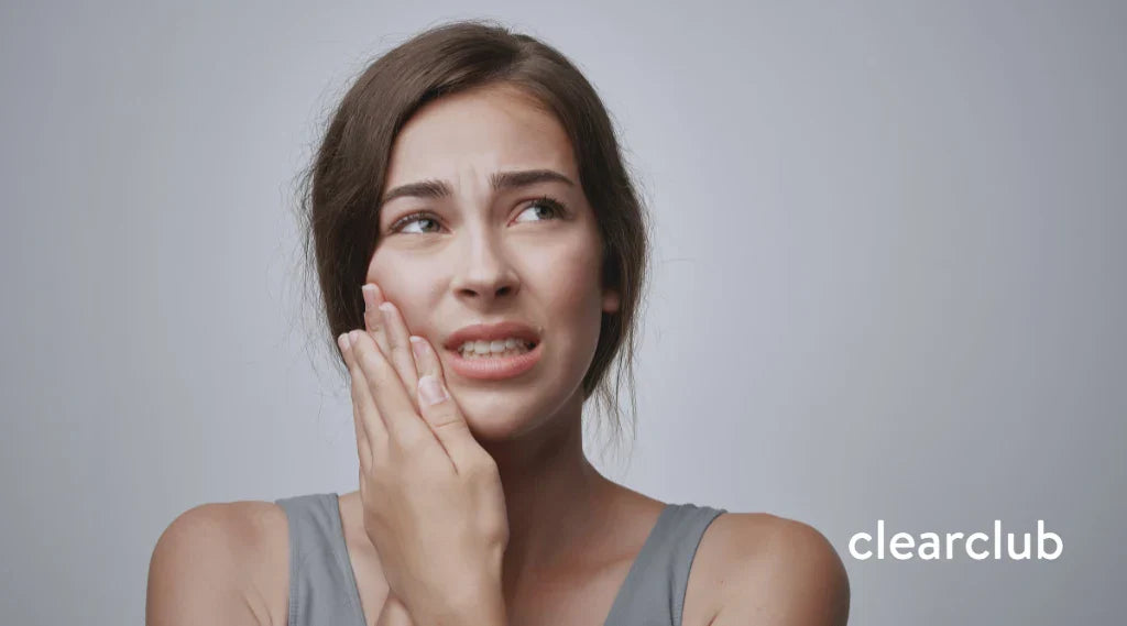 Woman holding her cheek with a pained expression, indicating discomfort caused by wearing retainers.